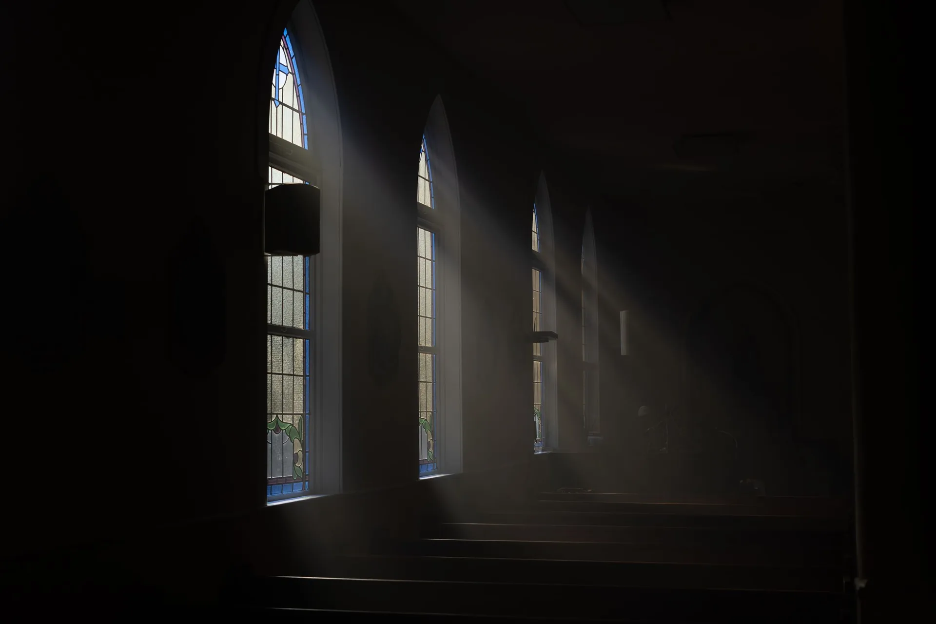 Soft daylight falling through tall arched windows into an empty, quiet chapel